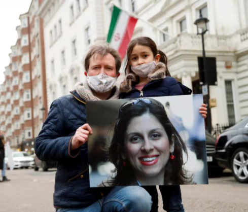 WAITING FOR MUMMY – Richard Ratcliffe stands with his six-year-old daughter, Gabriella, in front of the Iranian embassy in London March 8 as they tried to deliver a petition with more than 160,000 signatures calling for the immediate release of Gabriella’s mother, Nazanin Zaghari-Ratcliffe. They were turned away. A voice speaking over the embassy intercom refused even to open the door. Supporters of the family stood in front of the embassy with placards saying “Free Nazanin” and “Still Not Forgotten.”