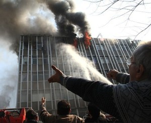 BLAZE — In shades of Asian sweatshops, a fired raged through a clothing factory in Tehran Sunday, killing two women who worked there as seamstresses—one of them seen here plunging to her death from the fifth story.  In the top photo, one woman cries from a window at left, while a man straddles a windowsill calling for help.  Another woman has climbed out the window and is clinging to the side of the building.  That woman then fell to her death, as seen in the middle photo.  It isn’t known if she lost her grip or could no longer hold on because of the heat.  Firefighters eventually got a ladder up to the building (bottom photo) and extracted the other people on the floor.