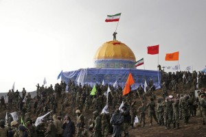 In this Friday, Nov. 20, 2015 photo released by the Tasnim News Agency, members of the Basij, the paramilitary unit of Iran's Revolutionary Guard, gather around a replica of Jerusalem's gold-topped Dome of the Rock mosque as one of them waves an Iranian flag from on top of the dome during a military exercise. Thousands of paramilitary forces from Iran's powerful Revolutionary Guard have held a war game simulating the capture of Jerusalem's Al-Aqsa Mosque from Israeli control, state media reported Saturday. (AP Photo/Tasnim News Agency, Mahmoud Hosseini)