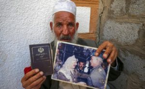 STUCK — Qassem Sheyasi holds up his expired passport from the Islamic Republic and a photo of him serving the late Yassir Arafat.