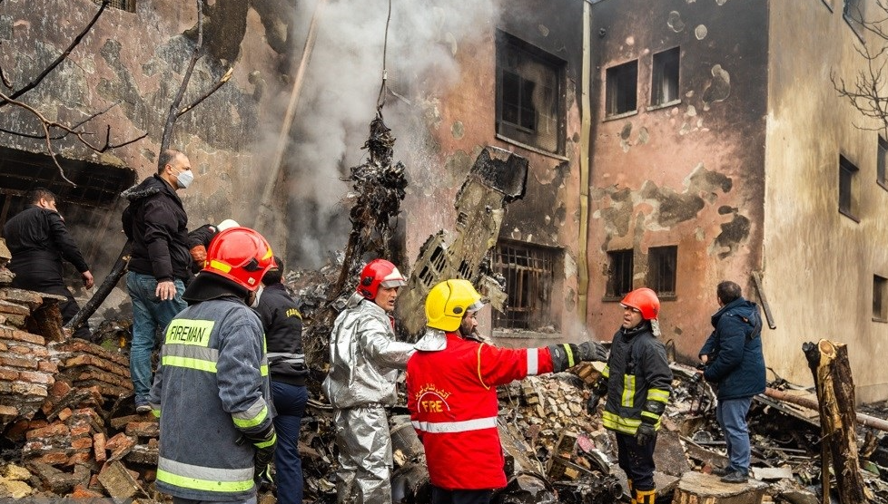 BURNING — The skeletal tail of the crashed jet can be seen over the head of the fireman wearing the yellow safety helmet.